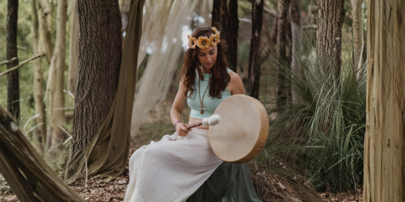 Tash playing her medicine drum in the Australian bush, surrounded by nature